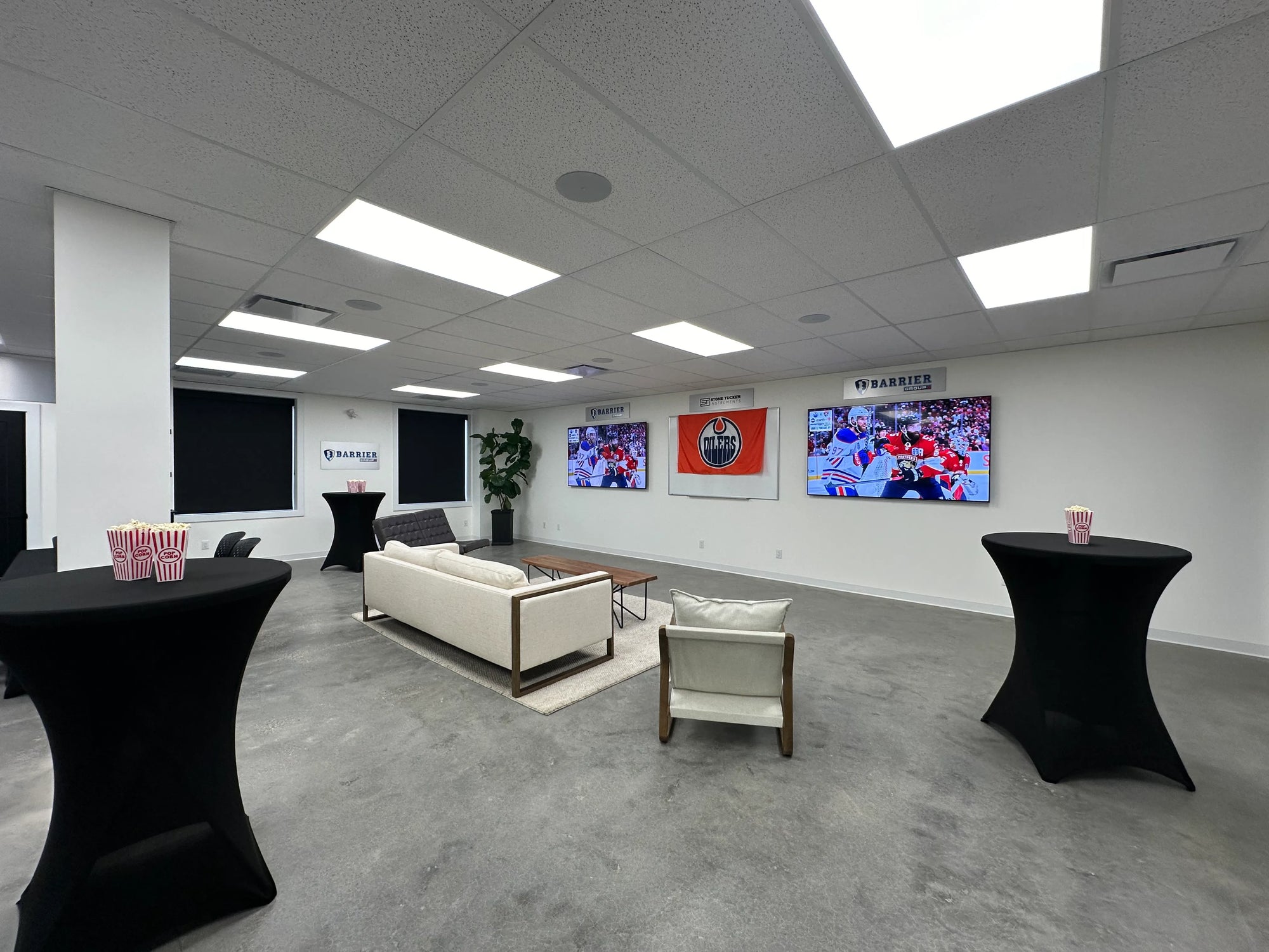 Couches and chairs set up in a room with two televisions playing a hockey game
